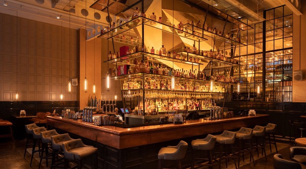 The illuminated central island bar inside The Alchemist, stocked with spirits under warm hanging lights.