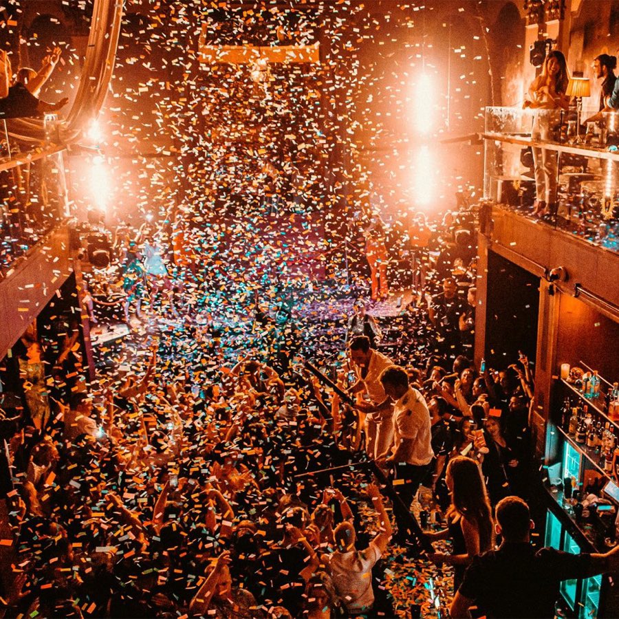 A packed venue floor at Alma under a shower of confetti and warm stage lighting during a live event.