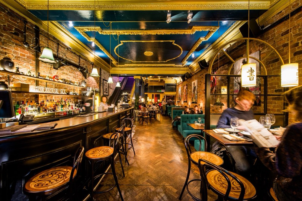 A characterful bar interior with exposed brick, a decorative ceiling and diners at candle-lit tables.