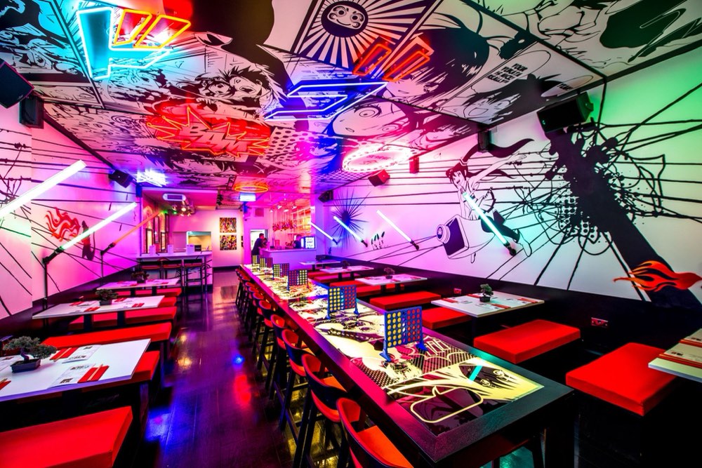 A vibrant neon-lit dining room with comic-book murals, red seating and long communal tables.