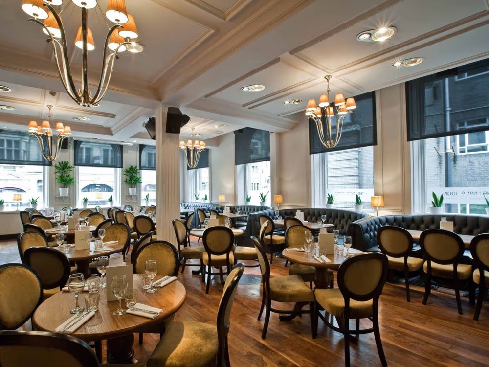 A grand brasserie dining room with a central spirits carousel, chandeliers and green leather booths.