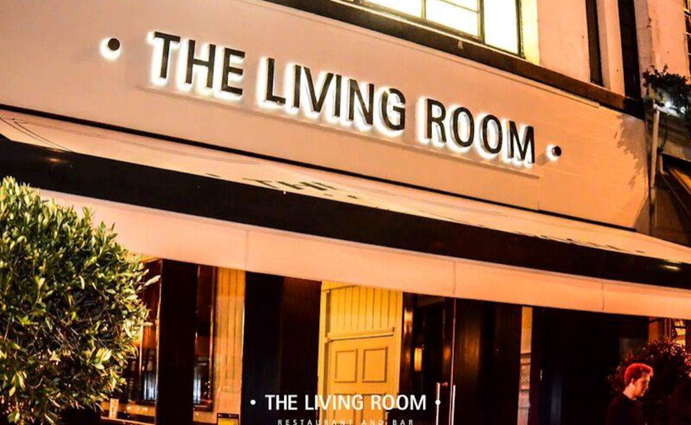 The illuminated exterior signage of The Living Room restaurant and bar at night.