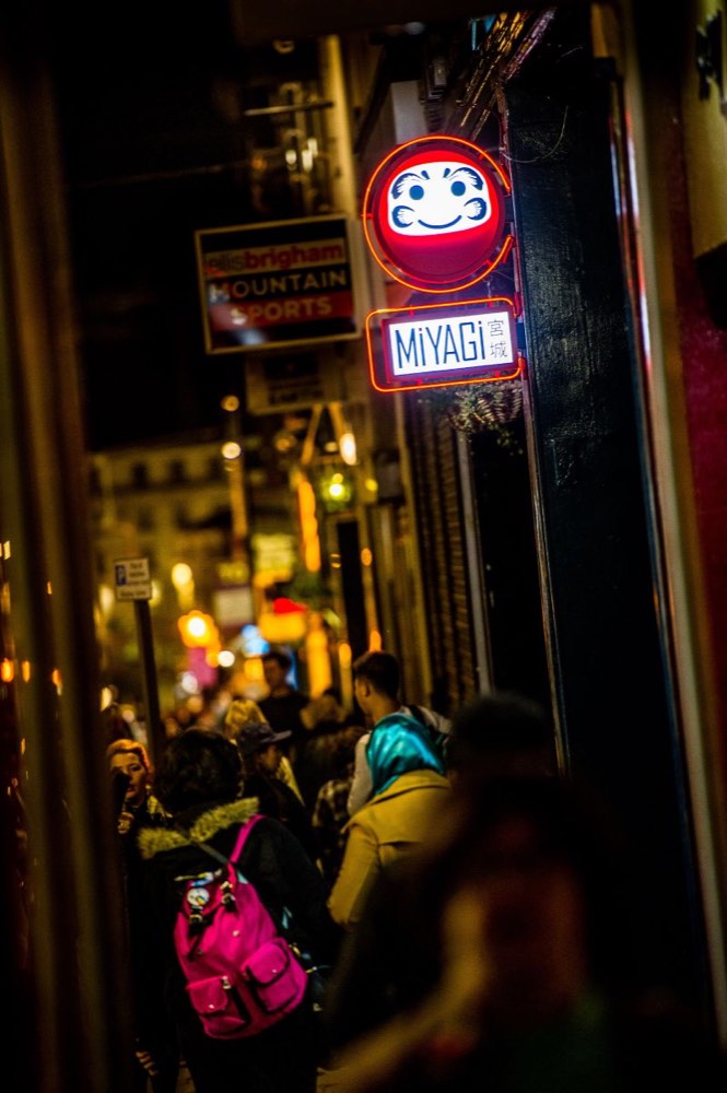 The glowing red Miyagi neon sign above a busy nightlife side street in Liverpool at night.